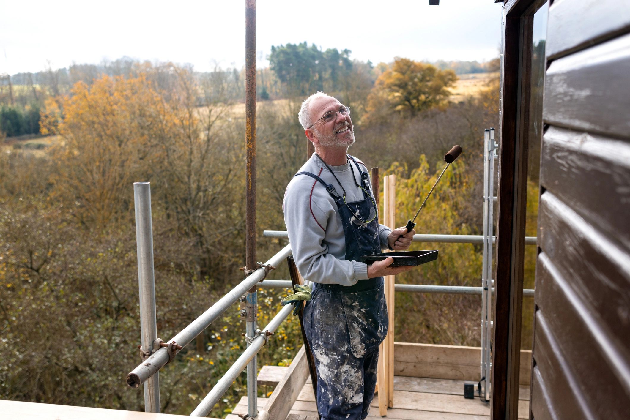 Friendly older handyman in a Mr Odd Jobs t-shirt painting the outside of a home